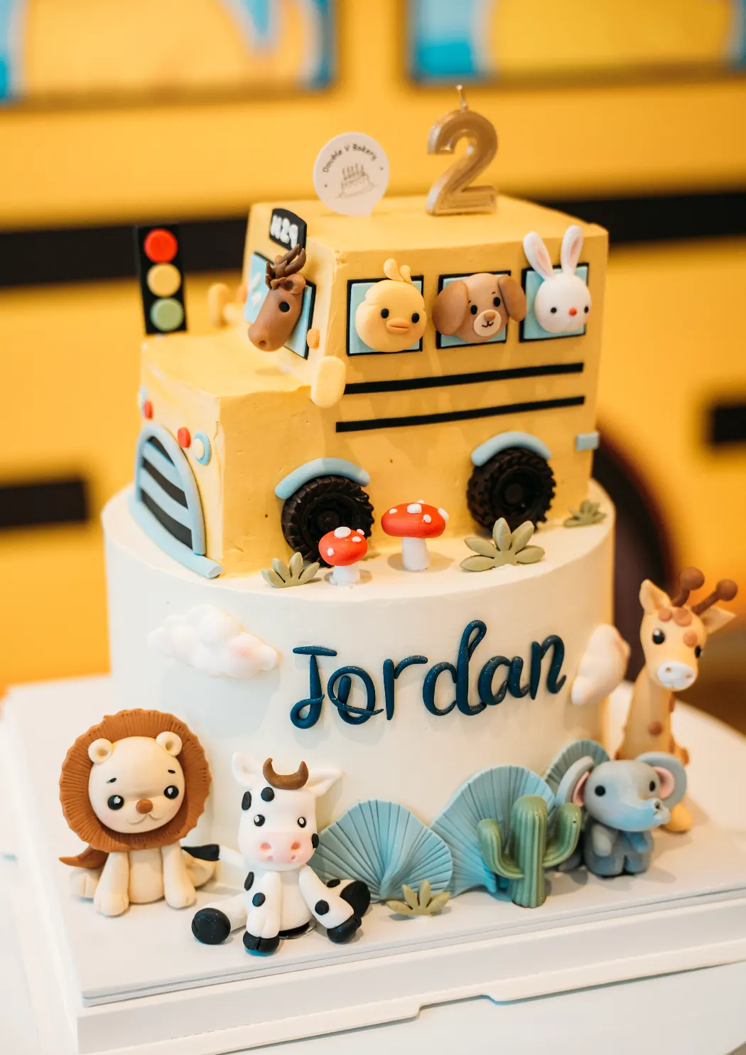 An 'Animals on the Bus' themed cake for Jordan's second birthday at Naru, with a number 2 candle and animal figures.