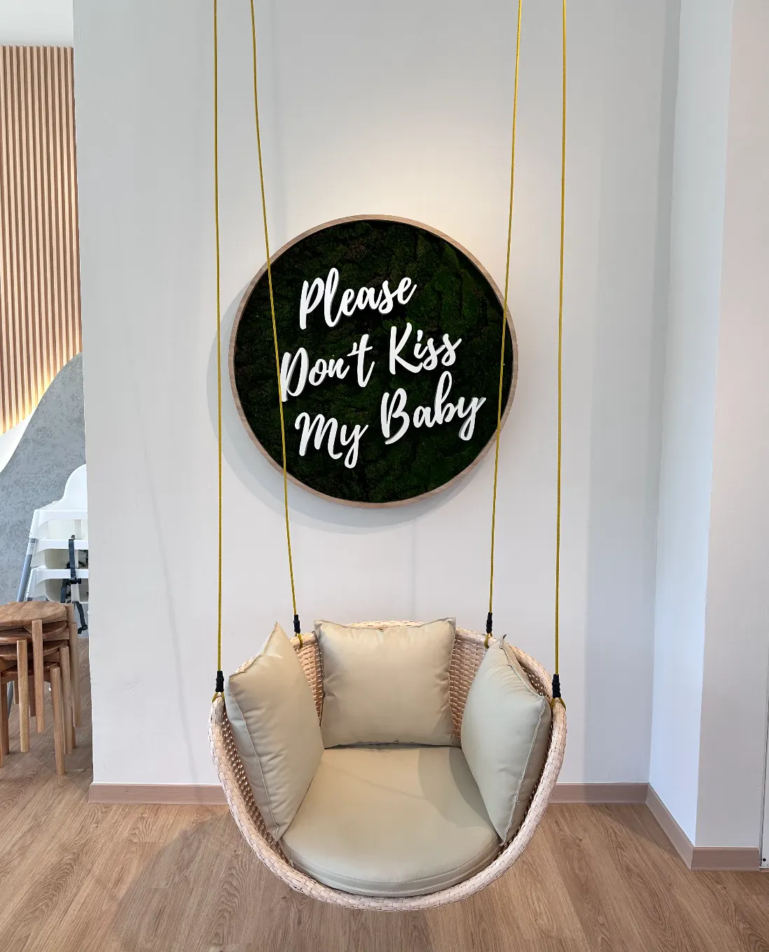 A round mossy 'Please Don't Kiss My Baby' sign hanging above a cosy swing chair photo corner at Naru.