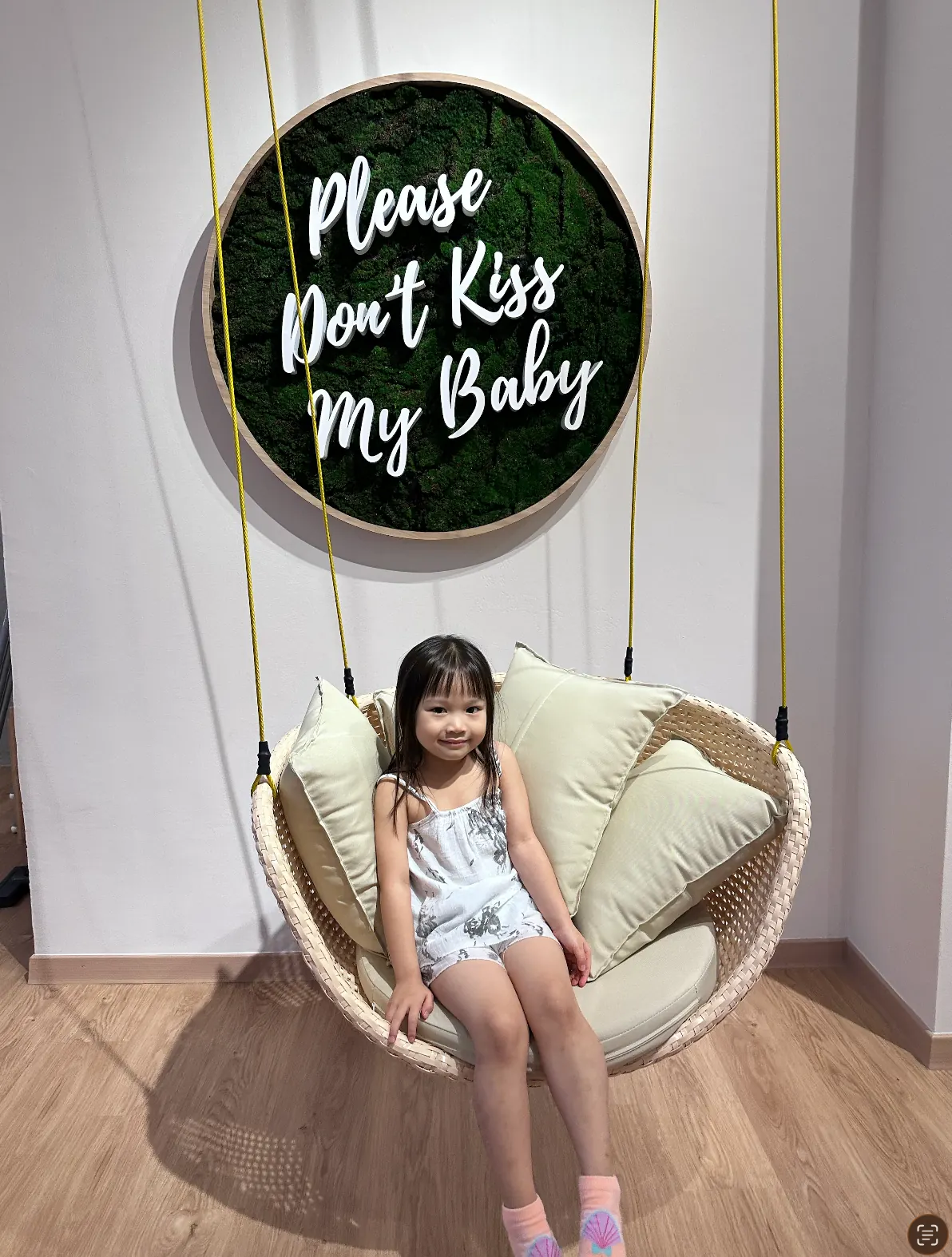 A young girl posing on the swing beneath the round 'Please Don't Kiss My Baby' sign at Naru.