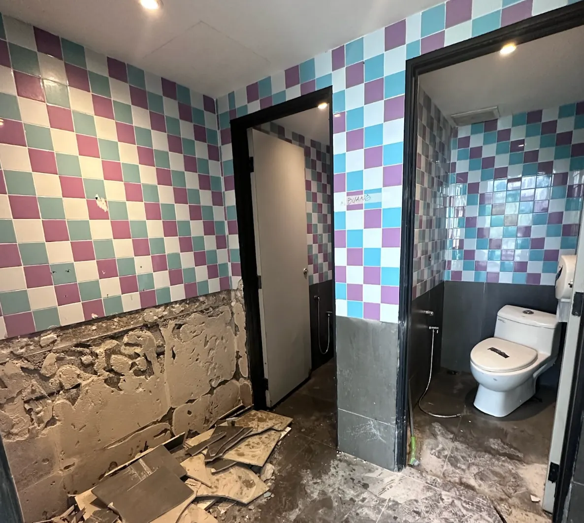 The unit's original bathroom mid-renovation — old checkered tiles and two standard cubicles, before the conversion.